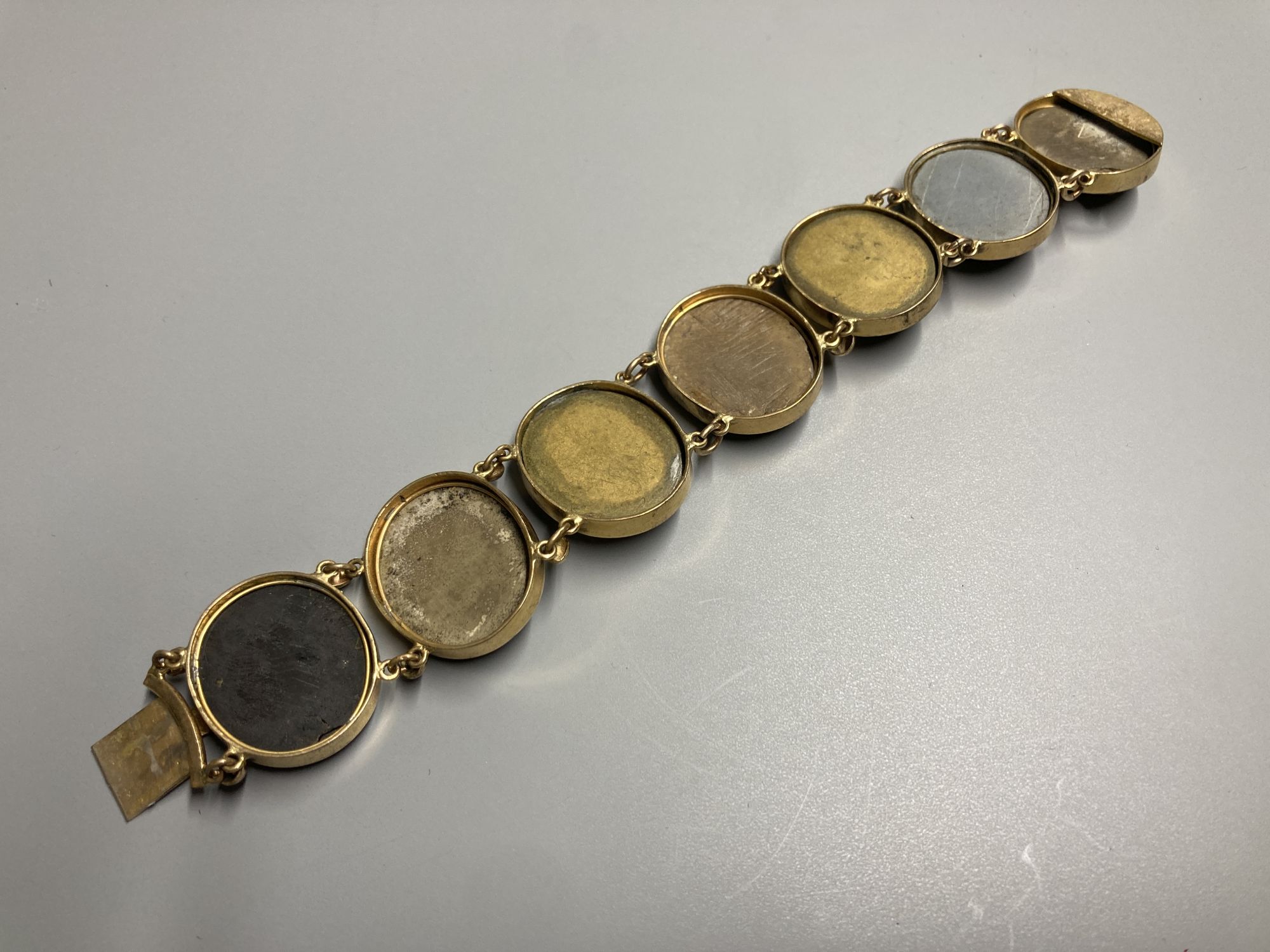 A late Victorian gilt metal bracelet set with seven oval lava plaques carved with busts of ladies, 17cm.